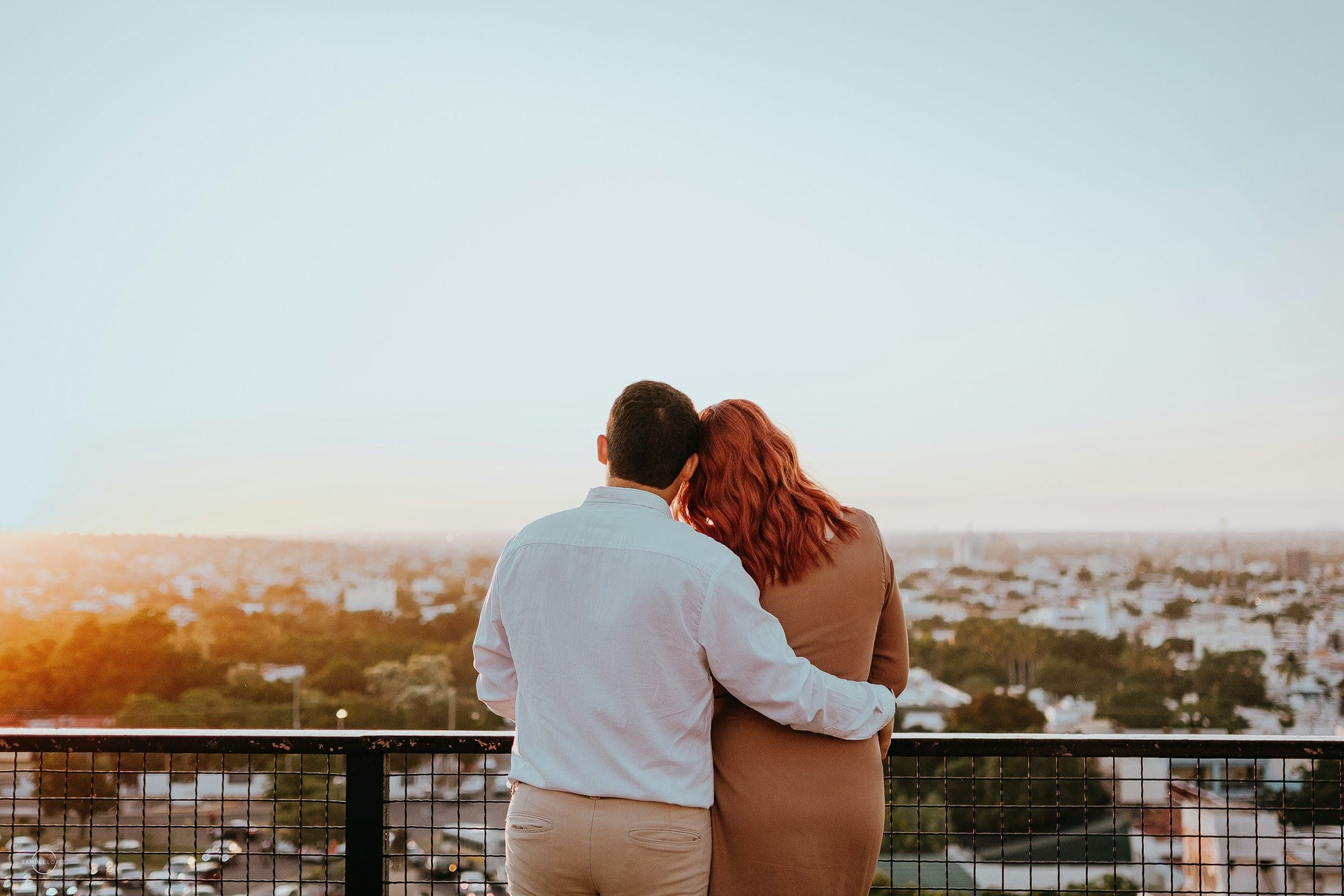 A couple embracing on a rooftop, looking out over the city in warm evening light