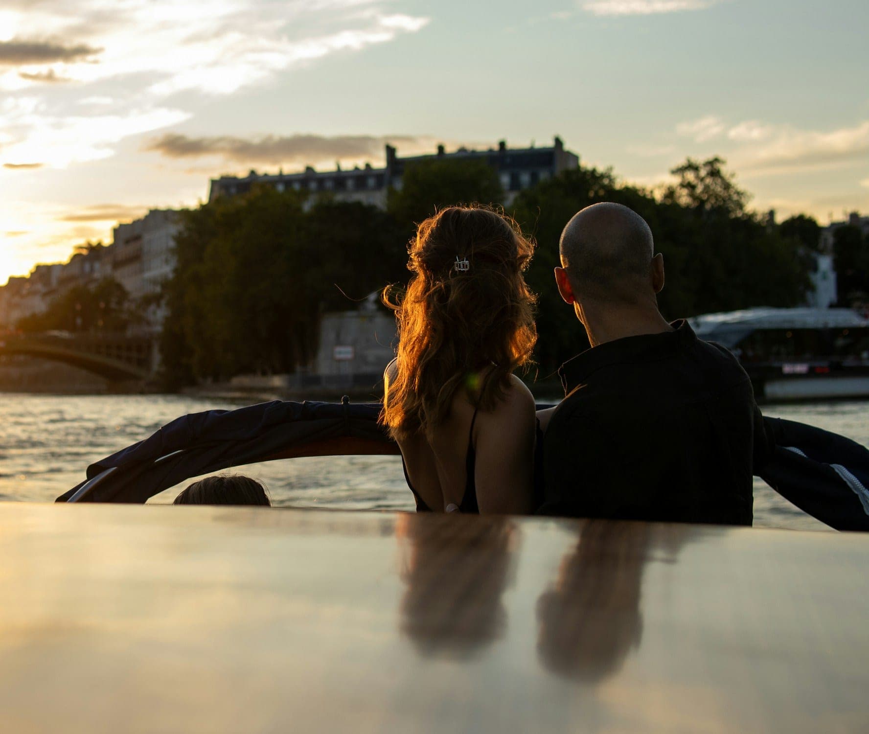 A couple on a wooden boat on the Seine in Paris, watching the sun set behind the city