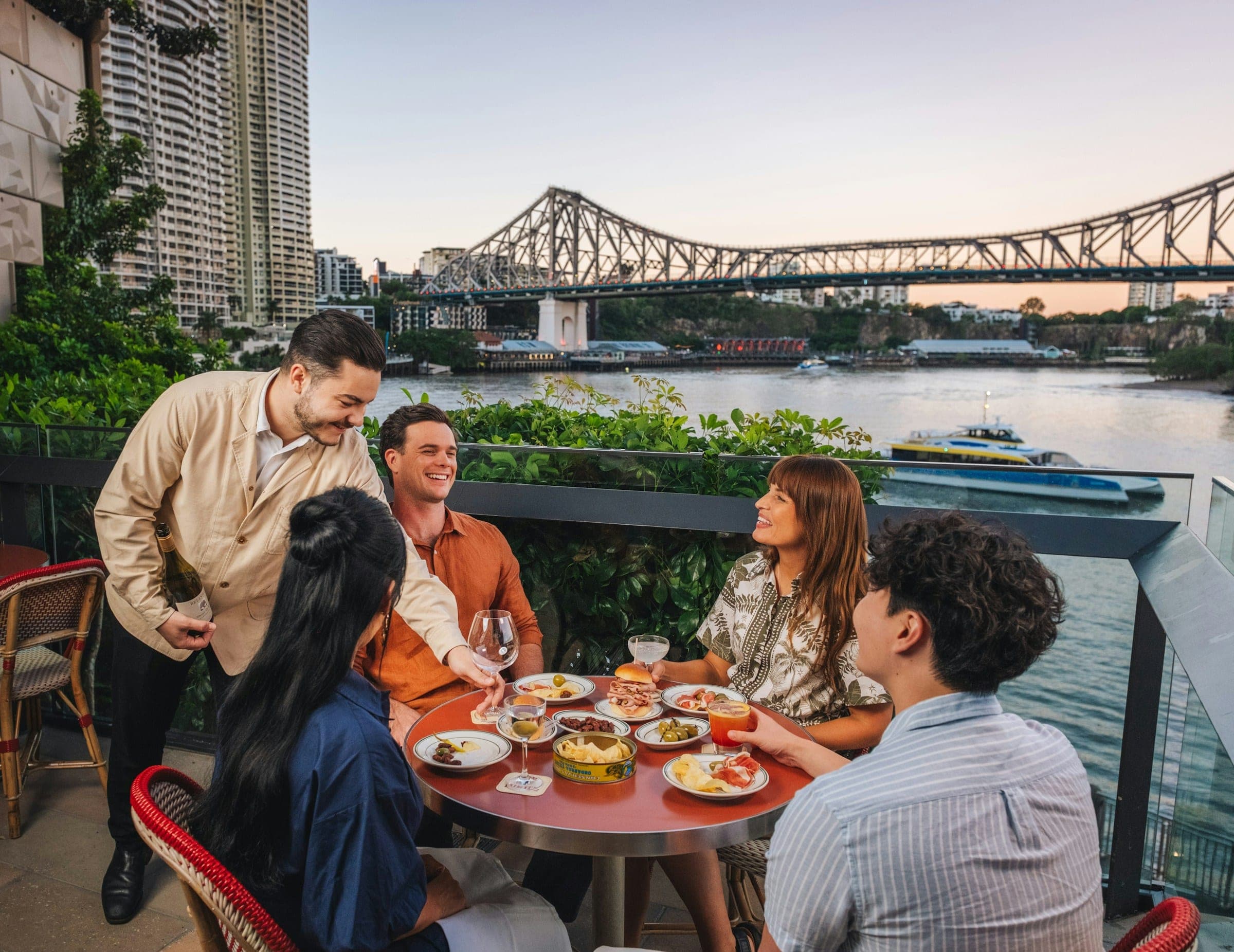 Friends sharing dinner and wine on a riverside terrace in the evening