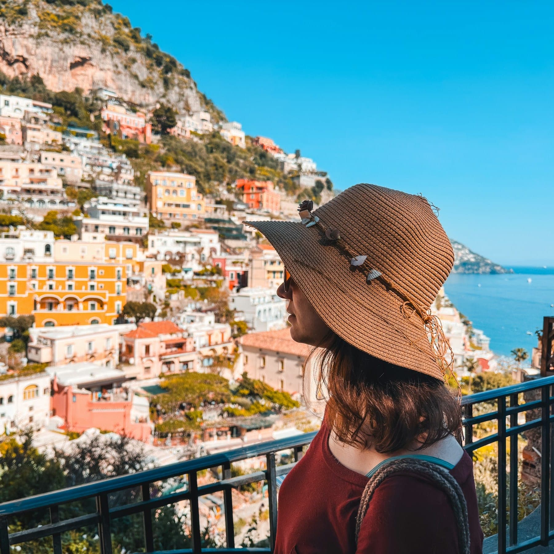 A woman in a sun hat looking out over Positano from a balcony: meet travellers whose plans match yours