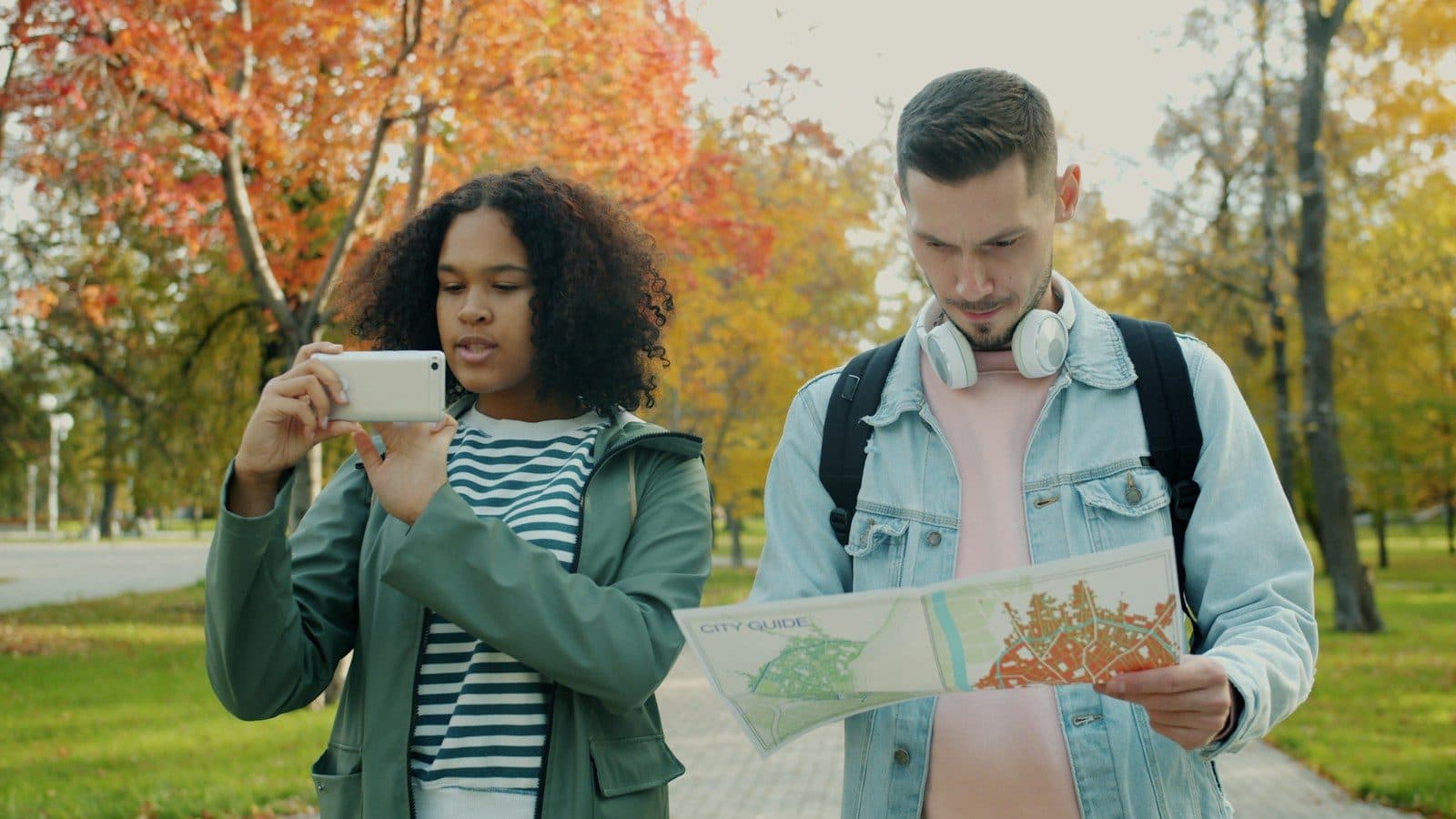 Two travellers planning a route with a map and a phone in an autumn park