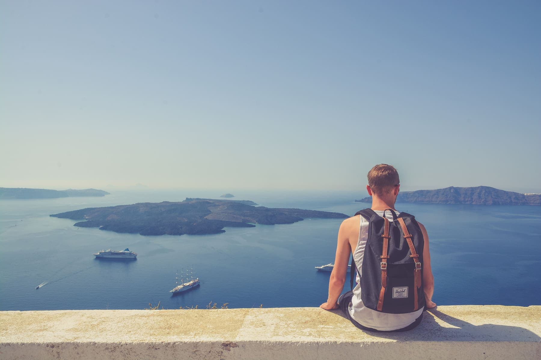 Traveler with a backpack sitting on a wall above the Santorini caldera