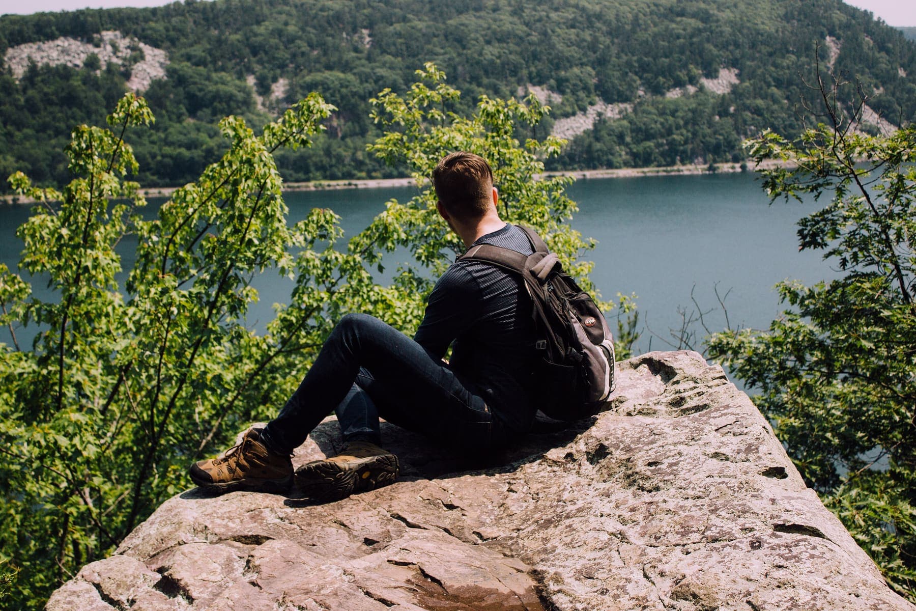 Backpacker sitting on a rock above a forested lake