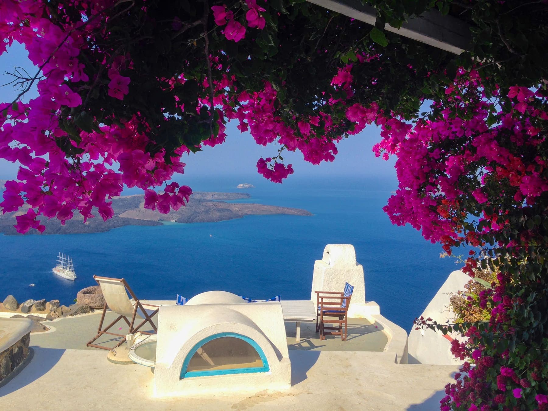 Pink bougainvillea framing a white terrace and the blue sea in Santorini