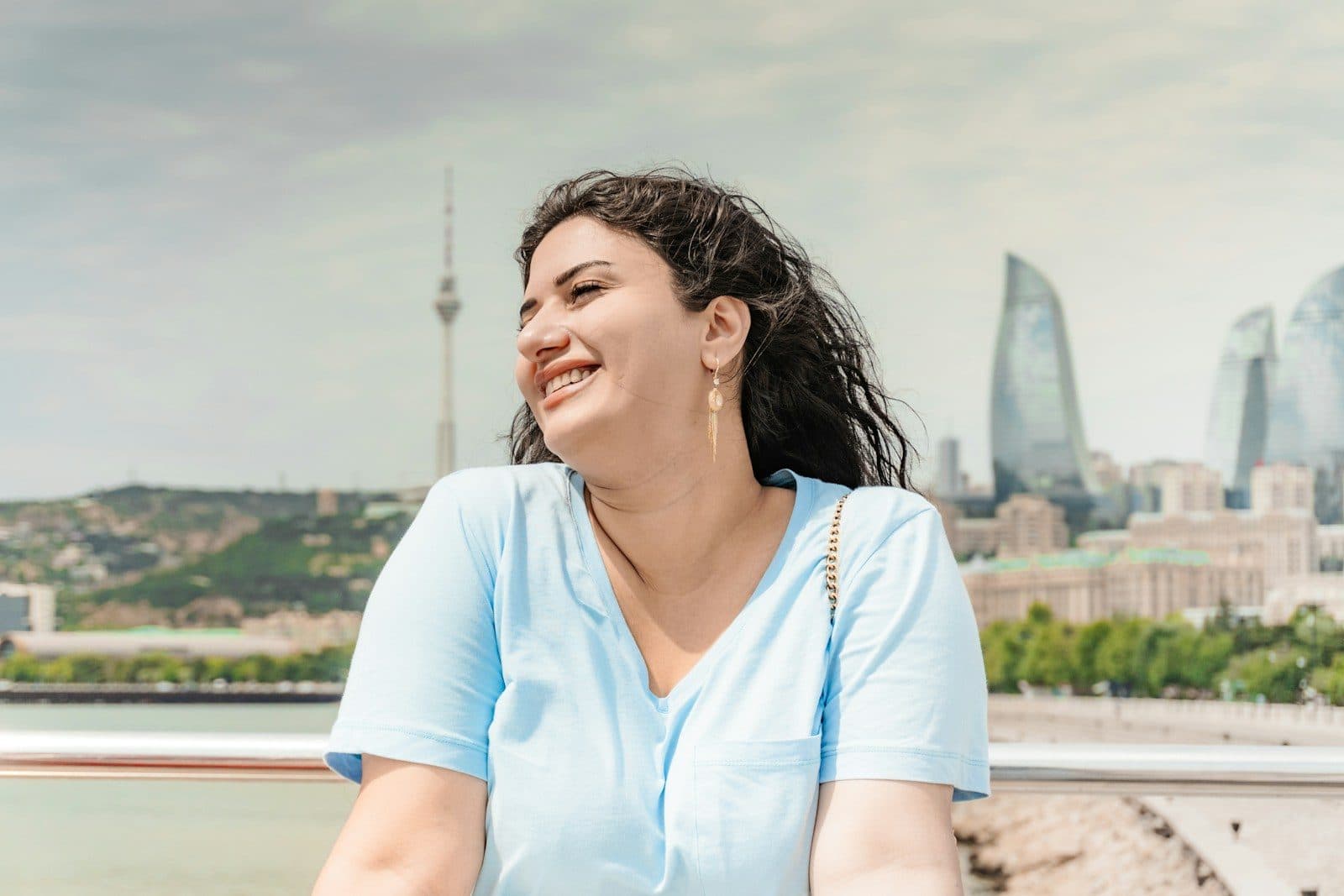 A smiling woman on a waterfront with a modern skyline