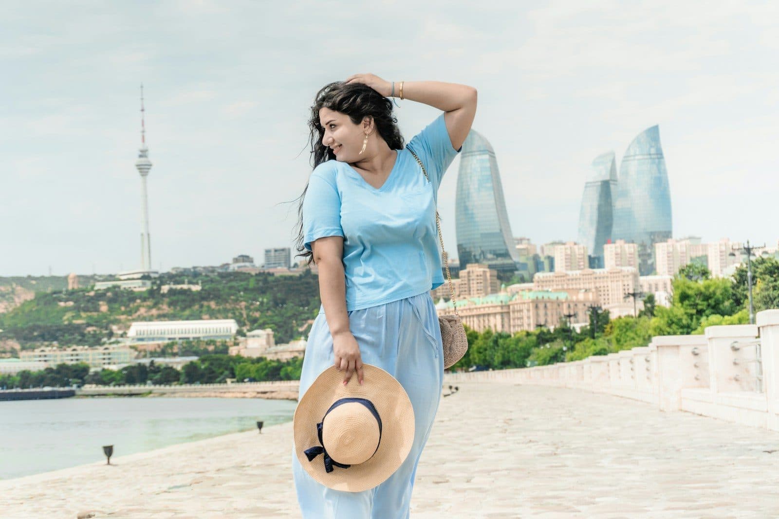 A smiling woman holding a sun hat with a city skyline behind her