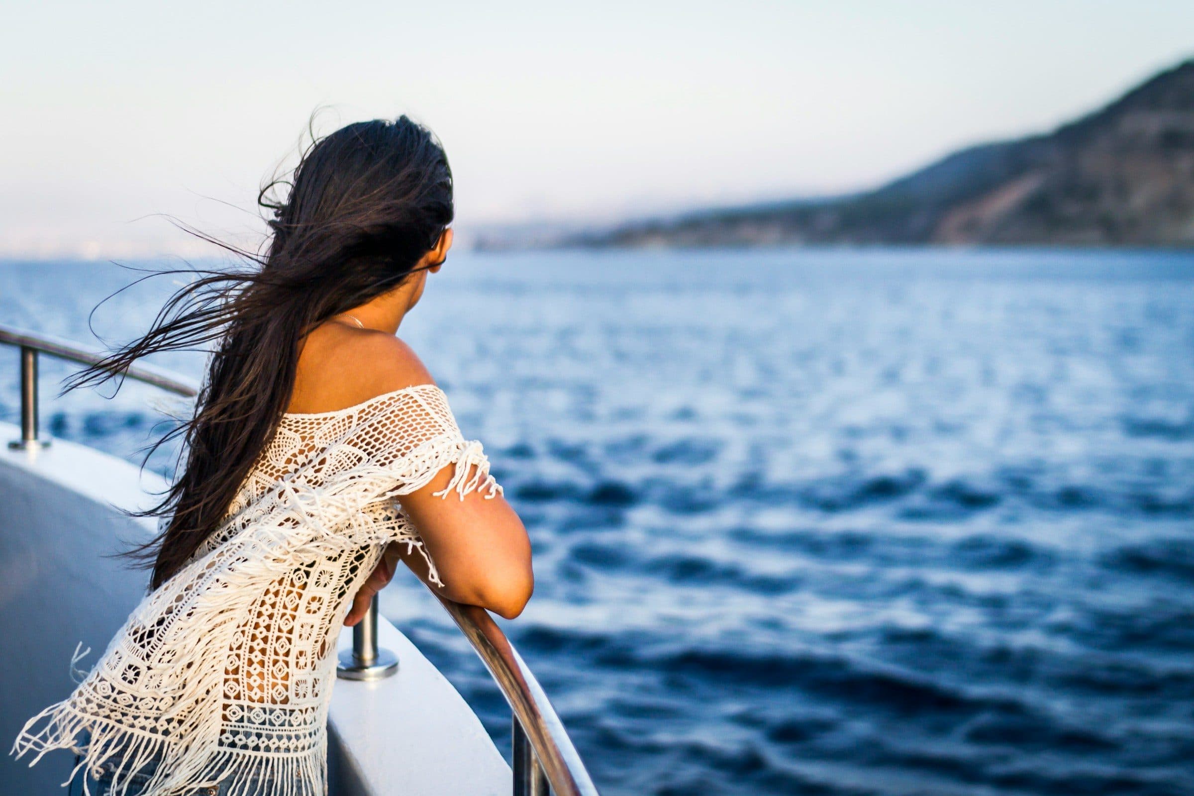 A woman with flowing hair at the rail of a boat, looking out over the Mediterranean